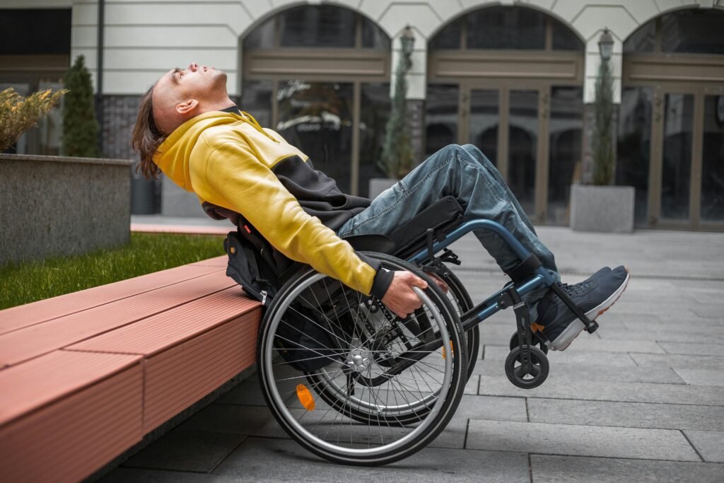 A young man in a hoodie relaxes in a wheelchair outside a modern building.